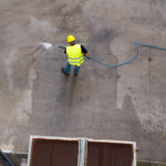 Man power washing cement ground. Photo has long hose. Man holding on to wand